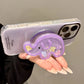 a woman holding a  phone with the kawaii cute elephant quicksand phone grip , this is in the color purple with colorful elephant faces inside, displaying it folds out and can be tilted to hold your phone on a flat surface, this is on a white background.