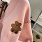 Sweet Teddy Bear Cardigan pastel pink edition with a bear sown into the chest area whilst the sleeves have large black stitches where they have been joined and black strips on the wrist cuffs and black and pink trim, this image is displaying a close up of the bear which is sitting with its arms open.