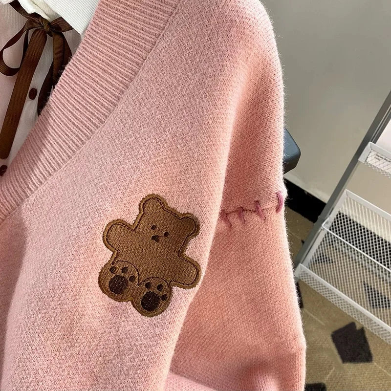 Sweet Teddy Bear Cardigan pastel pink edition with a bear sown into the chest area whilst the sleeves have large black stitches where they have been joined and black strips on the wrist cuffs and black and pink trim, this image is displaying a close up of the bear which is sitting with its arms open.