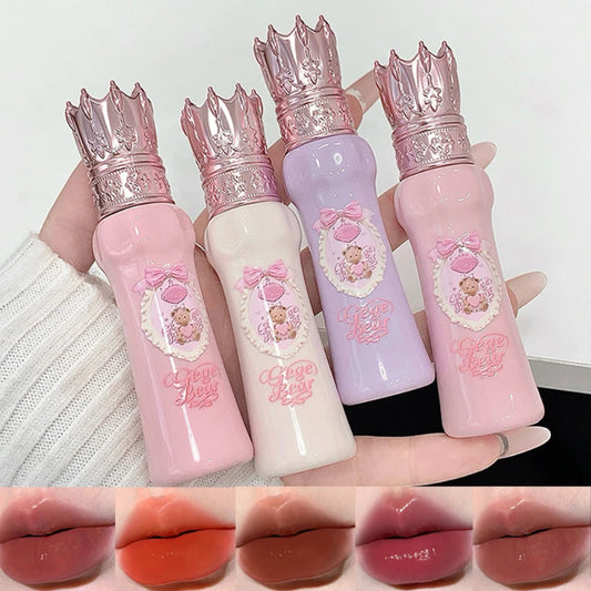 Set of four lip glosses with crowns on top, held by a hand against a white background.