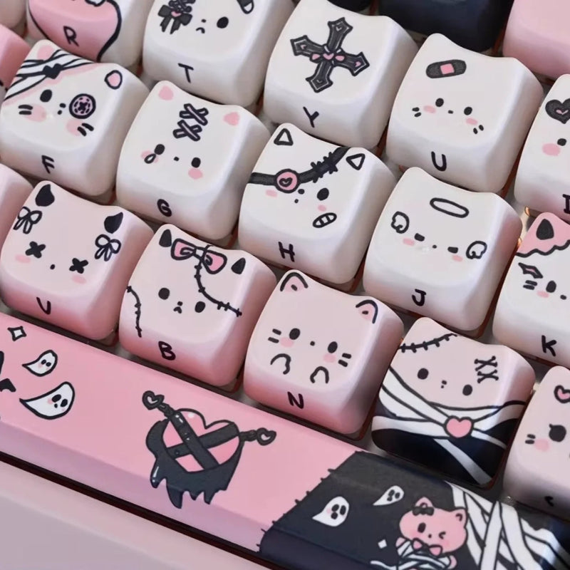 This image is showing a close up of the Kawaii Creepy Cuties Keyboard Keycaps, showing the designs on the keycaps such as cute cat faces  with skull necklace around their ear or bandages round their tiny tummies.