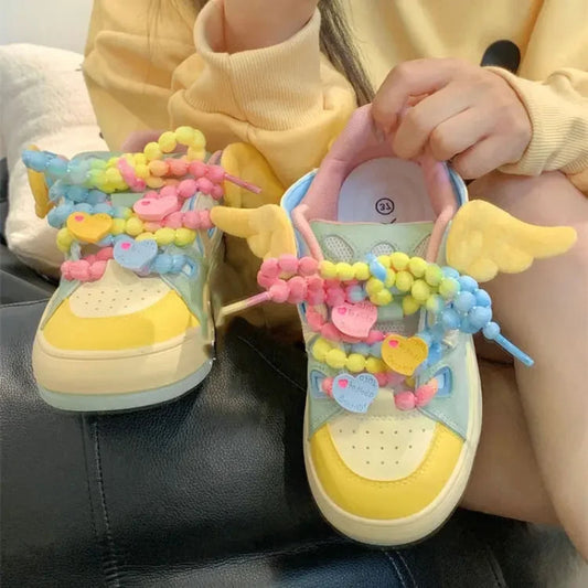 Angel on a rainbow platform sneakers, being displayed in front of a yellow hoodie and white wall.