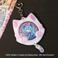 A pink cat-shaped Hatsune Miku keychain or card holder with a heart clasp and small attached charm, shown on a dark surface. The center displays an illustration of Hatsune Miku, with Japanese text including 'HATSUNE MIKU' and 'music camper'.