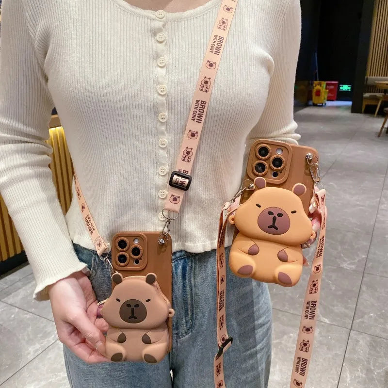 Person holding two Capybara -themed phone cases with a matching strap.