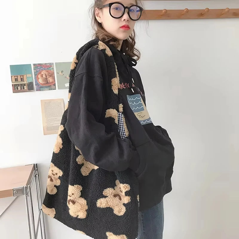 Person wearing a black jacket with teddy bear patterned tote bag in a room setting.
