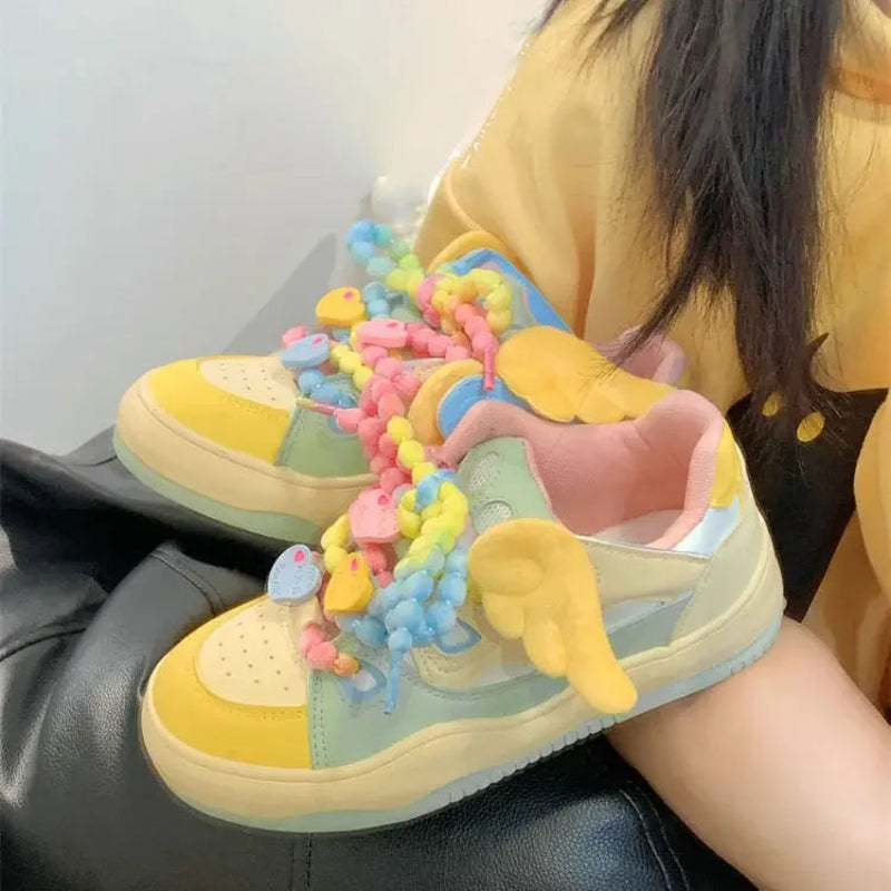 Angel on a rainbow platform sneakers, being displayed in front of a yellow hoodie and white wall.