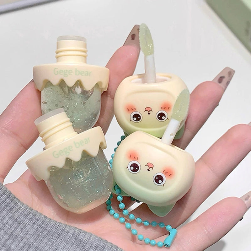 Two small, cute lip oil bottles with faces held in a hand against a light background