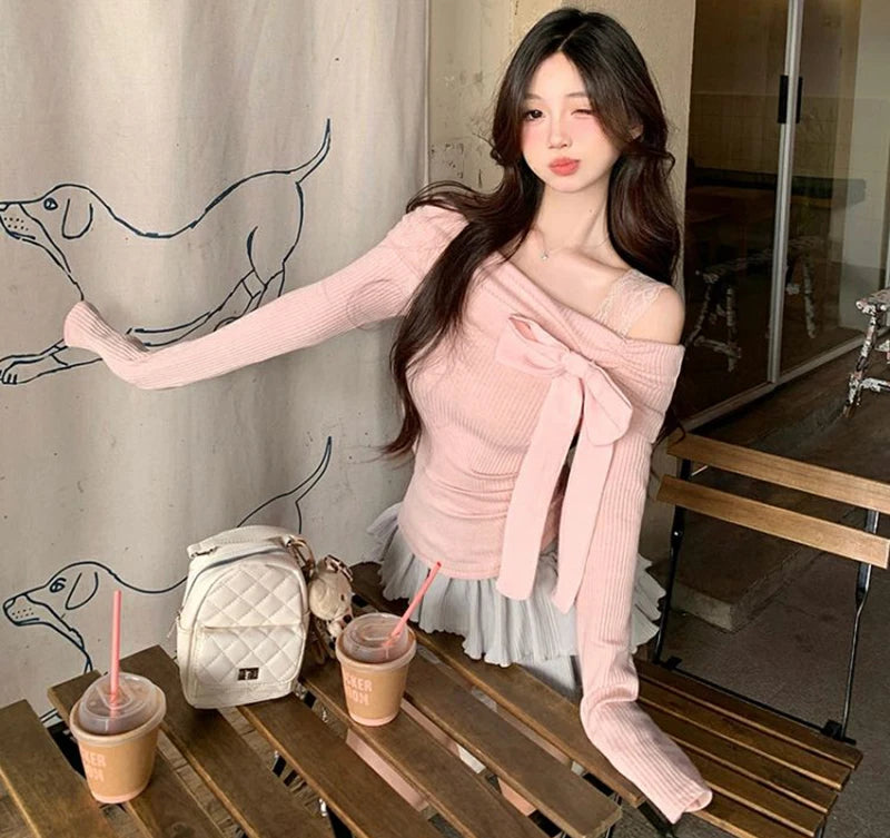 Woman wearing a pink shirt with a bow at a cafe table that has a small white backpack and two beverages.