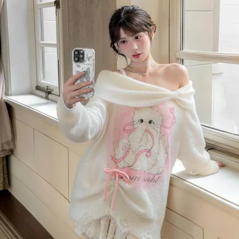 Woman wearing a white off-shoulder sweater with a cat design, standing by a window.
