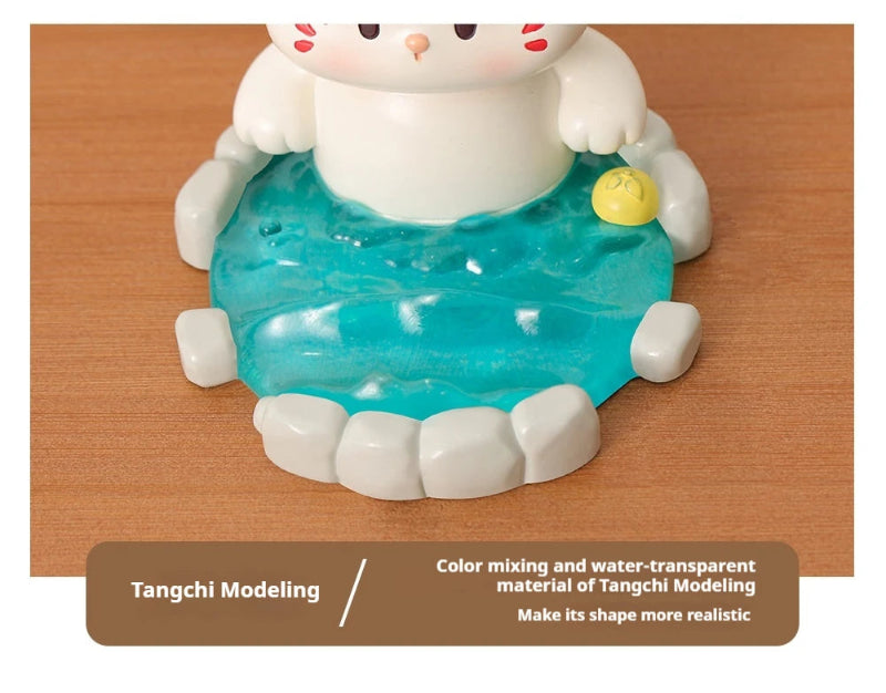 Cute resin figurine of a cat in a onsen with a yellow towel on its head on a wooden surface.
