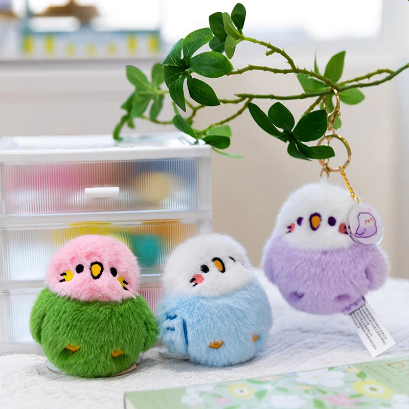 Three colorful bird plushie keychains on a surface with a branch poking from the side.