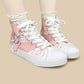 Pink high-top canvas sneakers with white laces, white rubber toe caps and soles, decorated with white cloud patterns and a silver bird graphic, shown on a model's feet against a beige background.