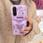 This image is showing Kawaii Butterfly Samsung Phone Case, one option is the purple design with a large 3D butterfly in the middle which is a phone grip with smaller butterflies around it and some white flowers.