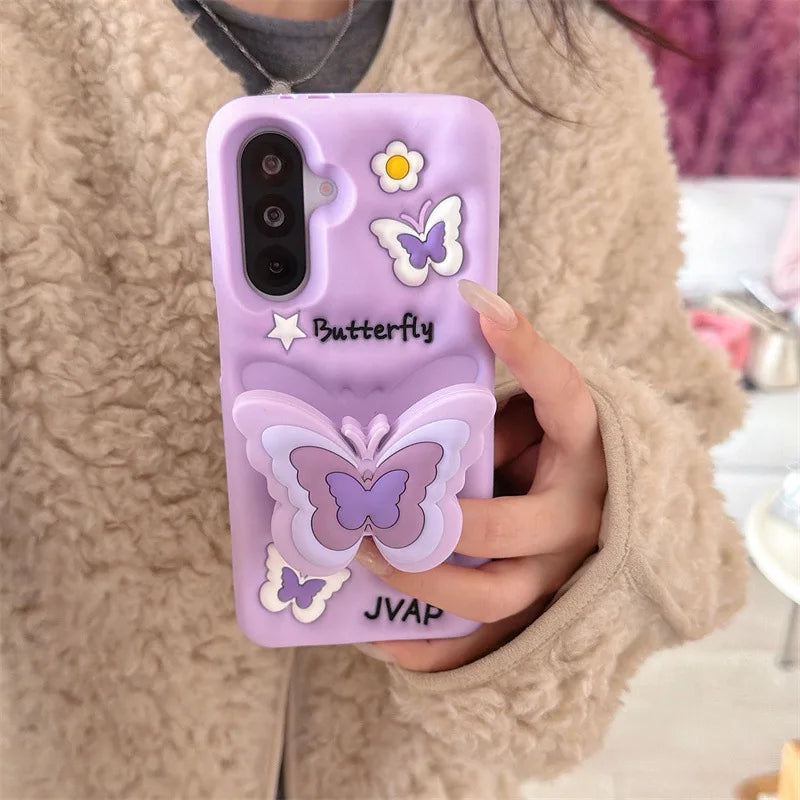 This image is showing Kawaii Butterfly Samsung Phone Case, one option is the purple design with a large 3D butterfly in the middle which is a phone grip with smaller butterflies around it and some white flowers.
