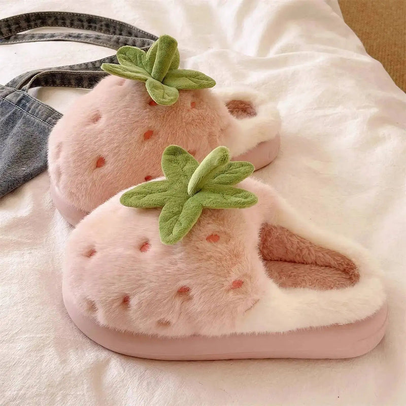 Pink strawberry-shaped slippers with green leaves on a soft surface.