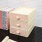 Three-tiered storage box with pink checkered design and heart shaped knobs on a reflective surface.