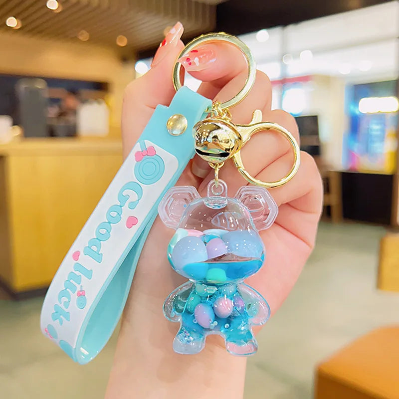 Hand holding a blue keychain with a transparent figure and 'Good Luck' tag in a blurred indoor setting.