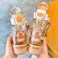 Two capybara themed water bottles held by a hand on a wooden surface.