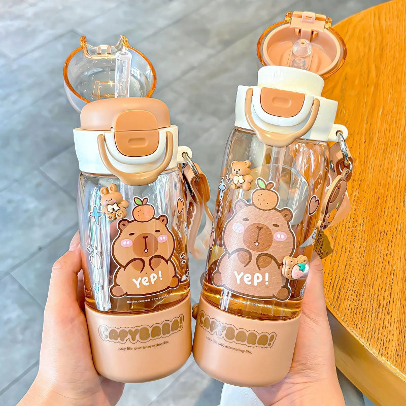 Two capybara themed water bottles held by a hand on a wooden surface.