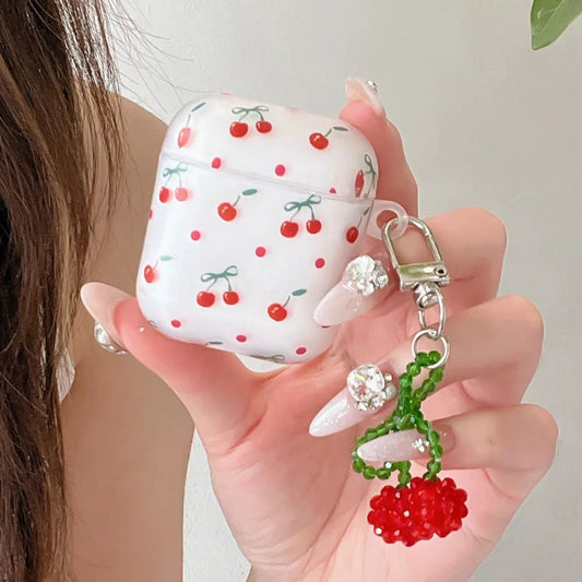 Hand holding a white AirPods case with red cherry pattern and a matching keychain.