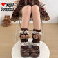 A person seated on a chair wearing decorative brown knit leg warmers with white lace ruffles and pom-poms, paired with dark brown bow shoes. A teddy bear sits on the floor in the background, and a TopJ Present logo appears in the top left corner.