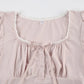 Close-up of a light pink top with lace trim on a white background