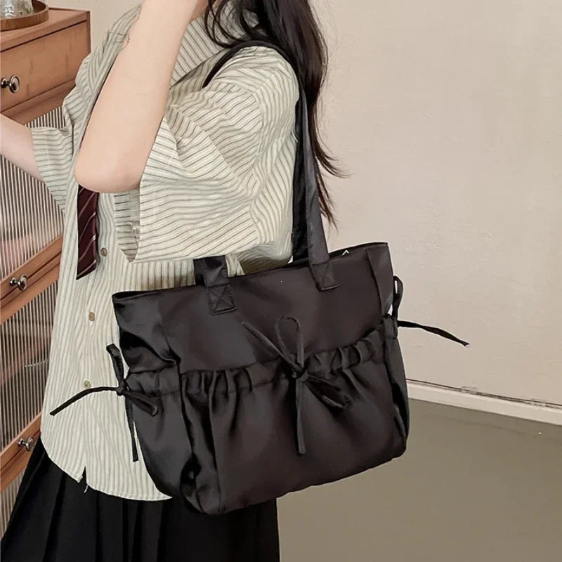 Person holding a black handbag with a bow detail indoors.