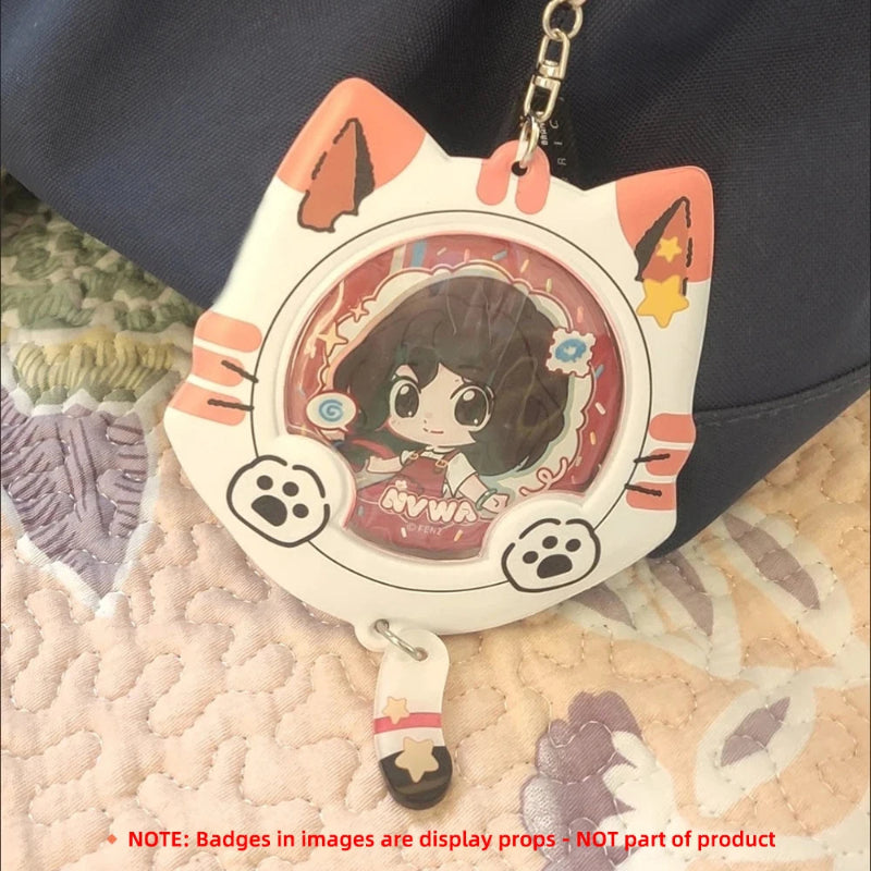 A cat-shaped acrylic keychain holder with a cartoon girl display insert, resting on a patterned quilt next to a dark navy bag. The keychain has orange paw-print accents, white cat ears, and a silver metal chain.