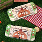 Two red panda-themed phone cases on grass with a checkered cloth in the background