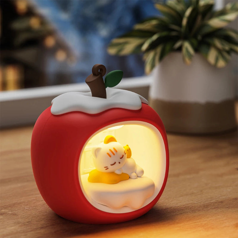 Decorative night light shaped like a red apple with a small Kawaii cat figure inside, resting on a yellow star pillow. on a wooden surface.