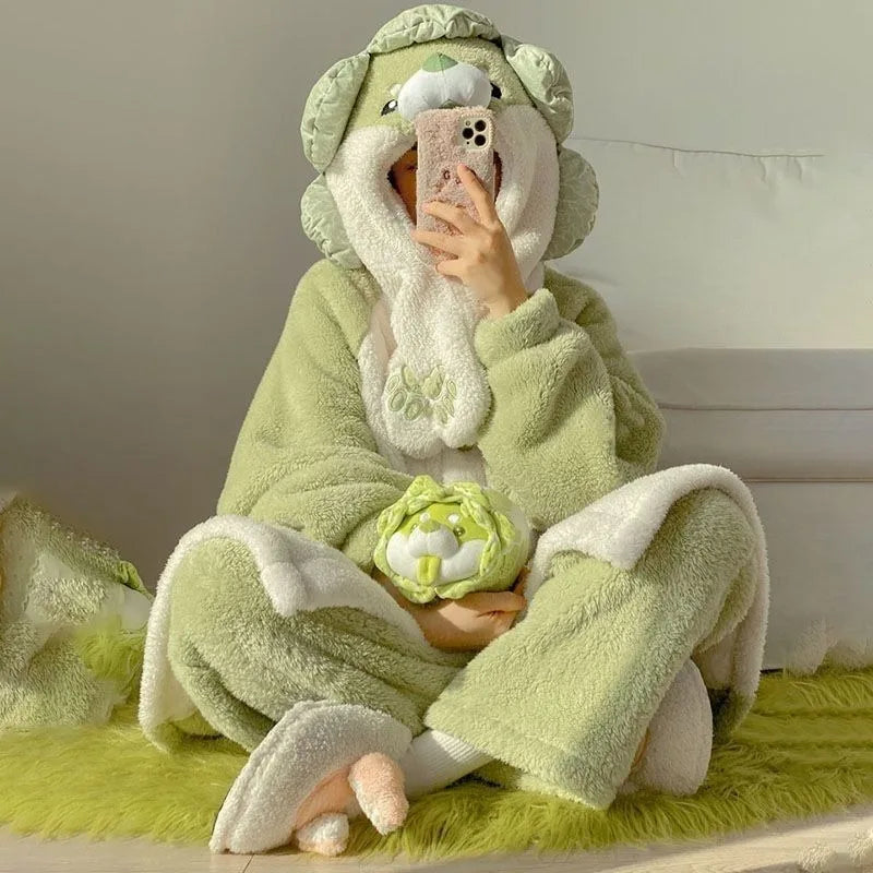 A person sitting cross-legged wearing a plush hooded animal onesie in pale green and white, holding a phone in front of their face while holding a small matching plush toy. The setting appears to be indoors on a bright yellow-green rug against a light wall.