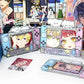 Three anime-themed Nintendo Switch-style standees and a small card are displayed on a white tabletop. The stands feature colorful character portraits, decorative cloud stickers, and game controller graphics.