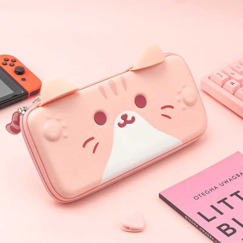 Pink cat-shaped Nintendo Switch case on a pink surface with a gaming console and book.