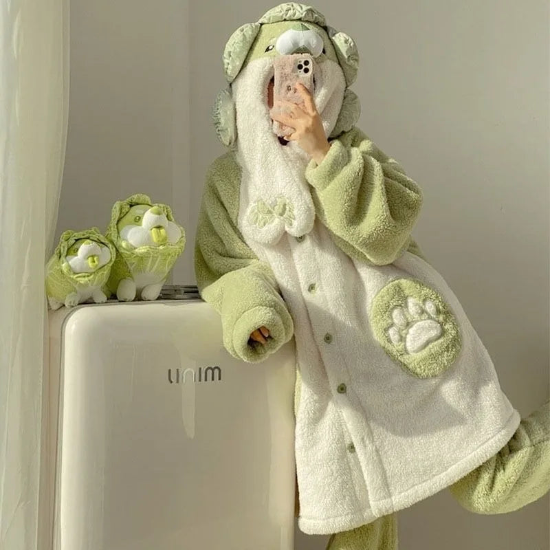 A person wearing a plush light green and off-white hooded robe with animal-inspired ear details and paw-print patches, taking a mirror selfie while leaning against a white appliance. Two matching plush accessories sit on the appliance beside them.