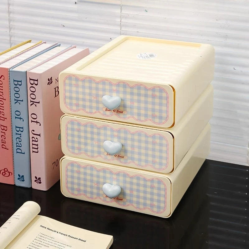 Three-tiered storage box with checkered design and heart-shaped handles on a surface with books.