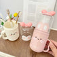Pink container with kawaii design on a wooden surface with a book and cup in the background.
