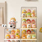 A collection of cute, pastel-colored collectible figurines displayed on clear acrylic shelves and a tabletop against a warm beige wall.