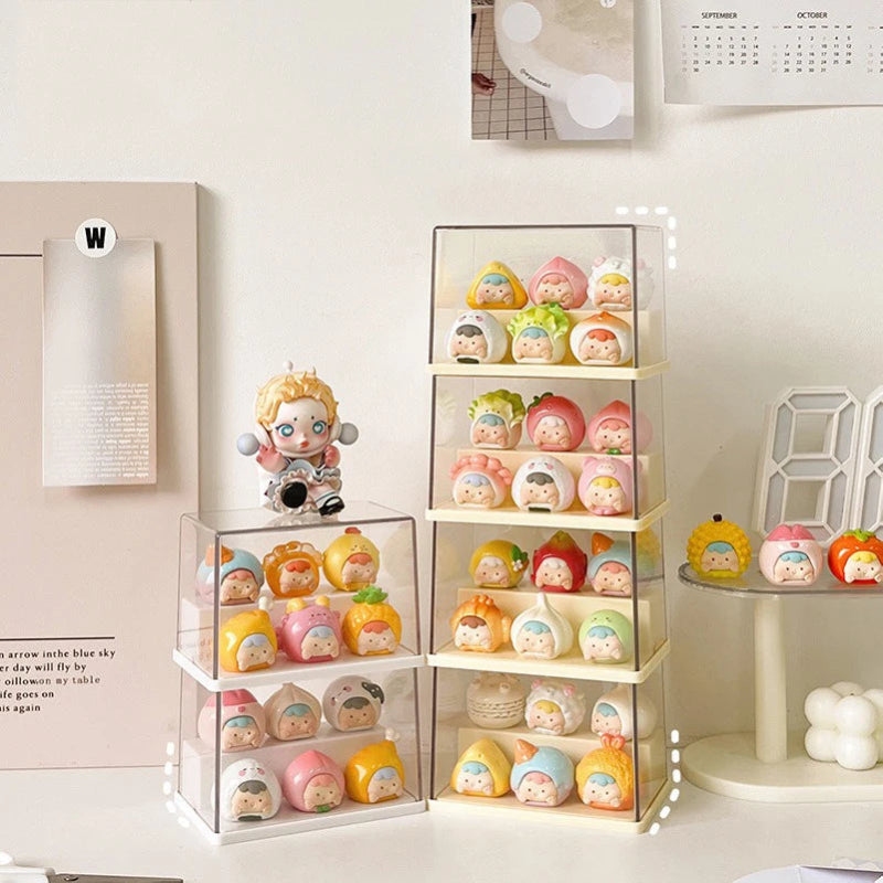 A set of clear acrylic blind-box display stands holding multiple small cartoon collectible figures, styled on a tabletop with decorative wall art and a calendar in the background.