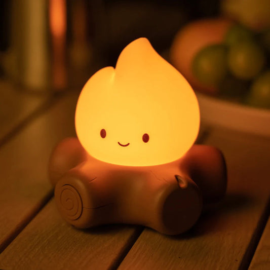 Small campfire night light with a smiling face on a wooden surface.
