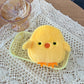 kawaii yellow plush chick coin purse on a textured white surface with a glass bowl in the background.