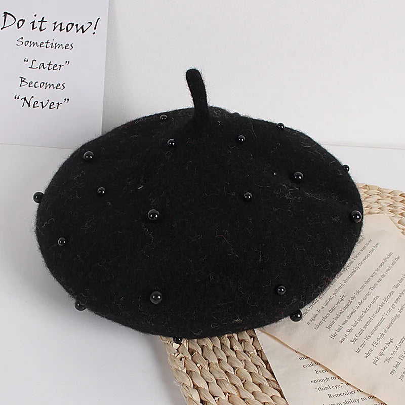 Black beret with bead embellishments on a textured surface with text in the background