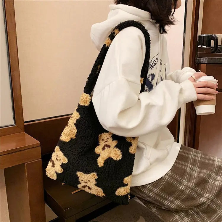 Person wearing a white hoodie and plaid skirt with a black and beige teddy bear patterned bag.