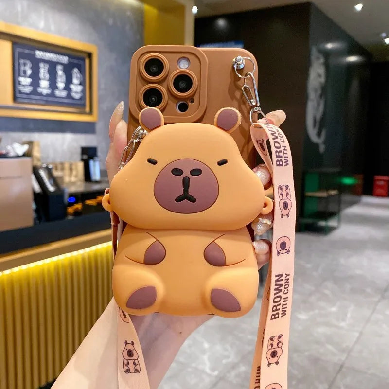 light brown capybara-shaped phone case with a lanyard held in front of a blurred cafe background