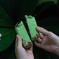 Green silicone keychain with kawaii design held by hands against a dark background