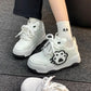 White sneakers with black paw print design worn on a gray carpet.