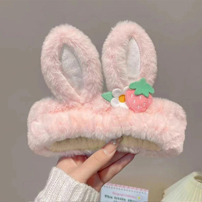 Pink fluffy bunny ears headband held by a hand against a neutral background
