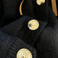 Sweet Teddy Bear Cardigan black edition with a bear sown into the chest area whilst the sleeves have large white stitches where they have been joined and black strips on the wrist cuffs with white, black and white trim. This image is a close up of the dappled buttons