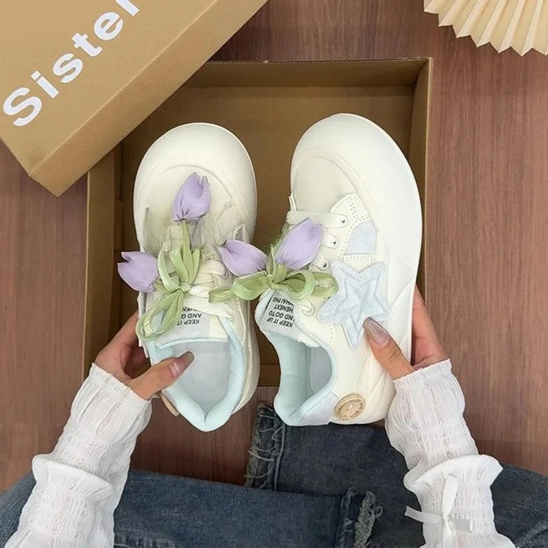 White sneakers with floral decorations held by a person, with a 'Sister' box in the background.