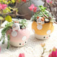 Two cute mushroom-shaped planters with animal figures on a textured surface.