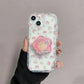 A woman is holding one of the designs available for the Kawaii Cherry Blossom Samsung Phone Case, this design is petite floral patter design with a large cherry blossom phone grip that attaches to it.